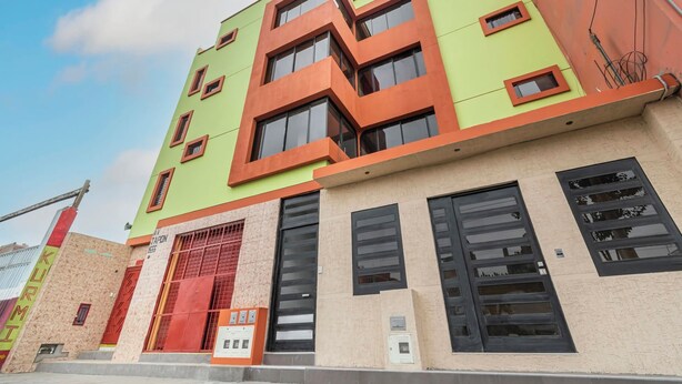 A multi-story building with a green and orange facade, large windows, and a visible entrance with a red door. - Kurmi House Lima Airport (Callao)