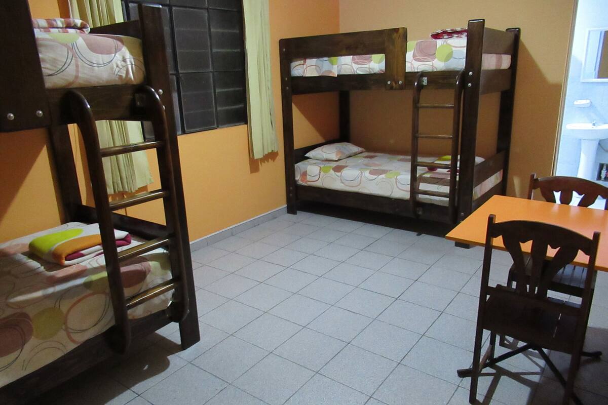 A dormitory room with bunk beds, a wooden table, and chairs.