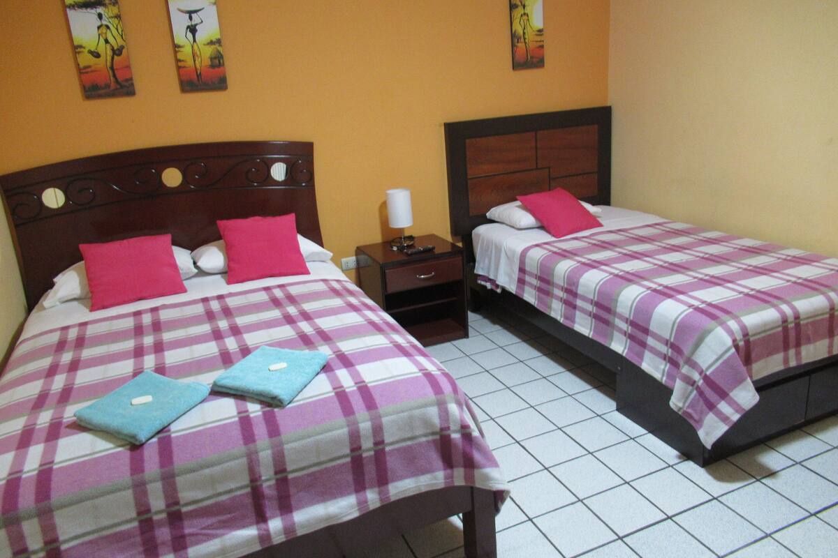 Two double beds with plaid bedding, wooden headboards, and pink pillows.