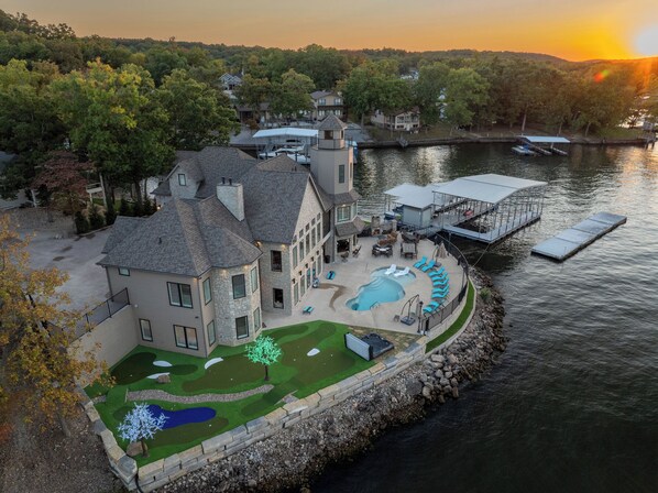 A lakeside property with a swimming pool, dock, and well-maintained lawn.