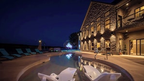 Uma área de piscina com espreguiçadeiras e um edifício de pedra com várias janelas e varandas.