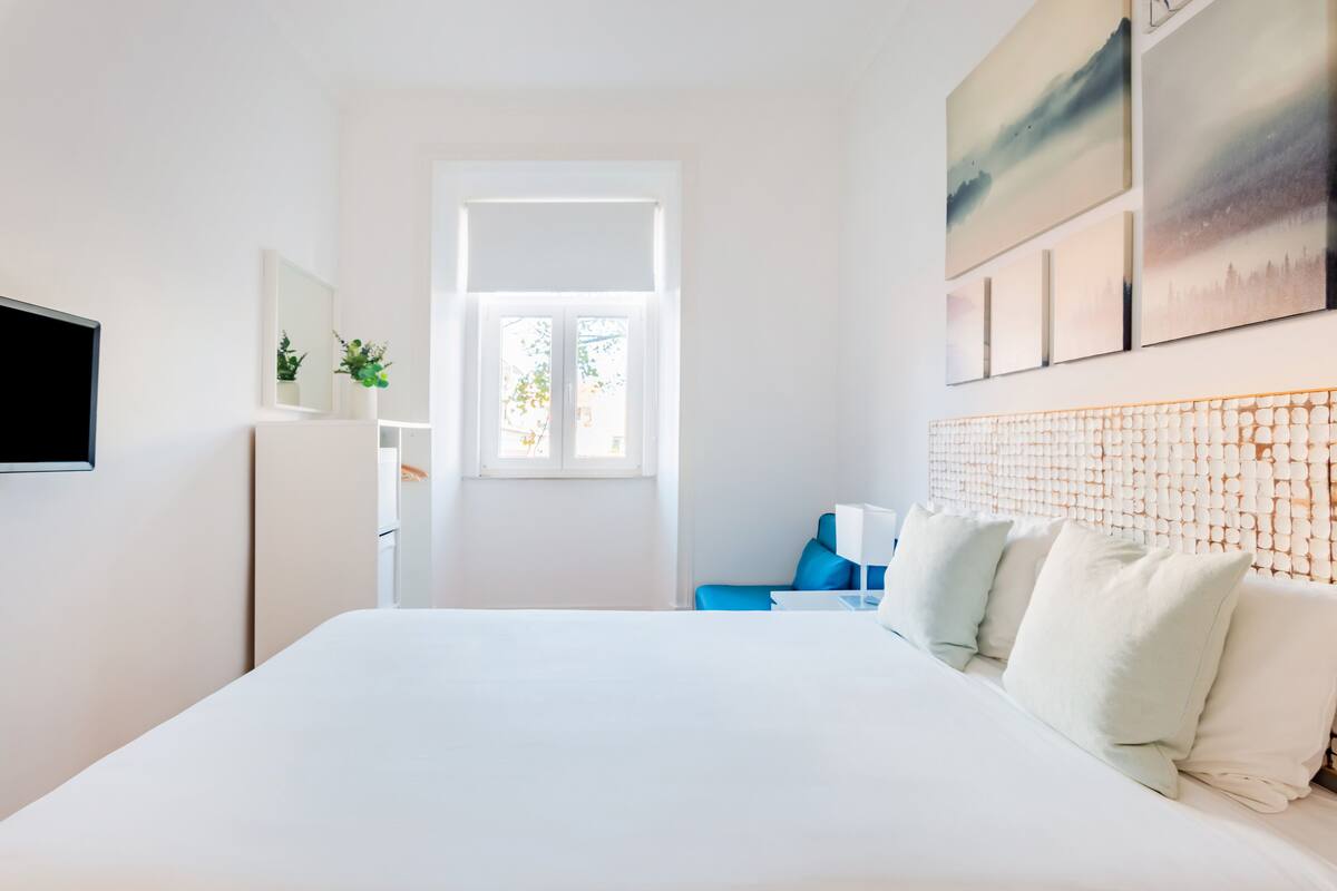 Ein modernes Hotelzimmer mit einem großen Bett, einem Schreibtisch mit Stuhl, einem Flachbildfernseher und Bildern an den Wänden.