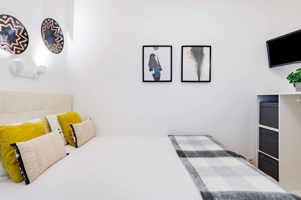 Ein Schlafzimmer mit Bett, Kissen, Nachttisch, Fernseher und Wandbildern.
