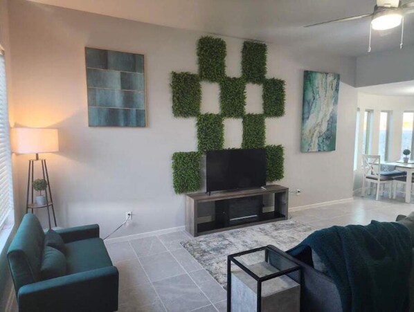 Un salon avec un téléviseur, un canapé, une lampe et un tableau au mur.