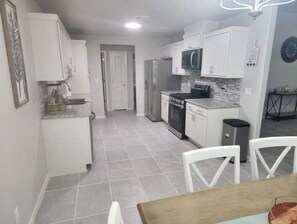 Une cuisine moderne avec des meubles blancs, un four à micro-ondes et une cuisinière. On y trouve également un coin repas avec une table et des chaises.