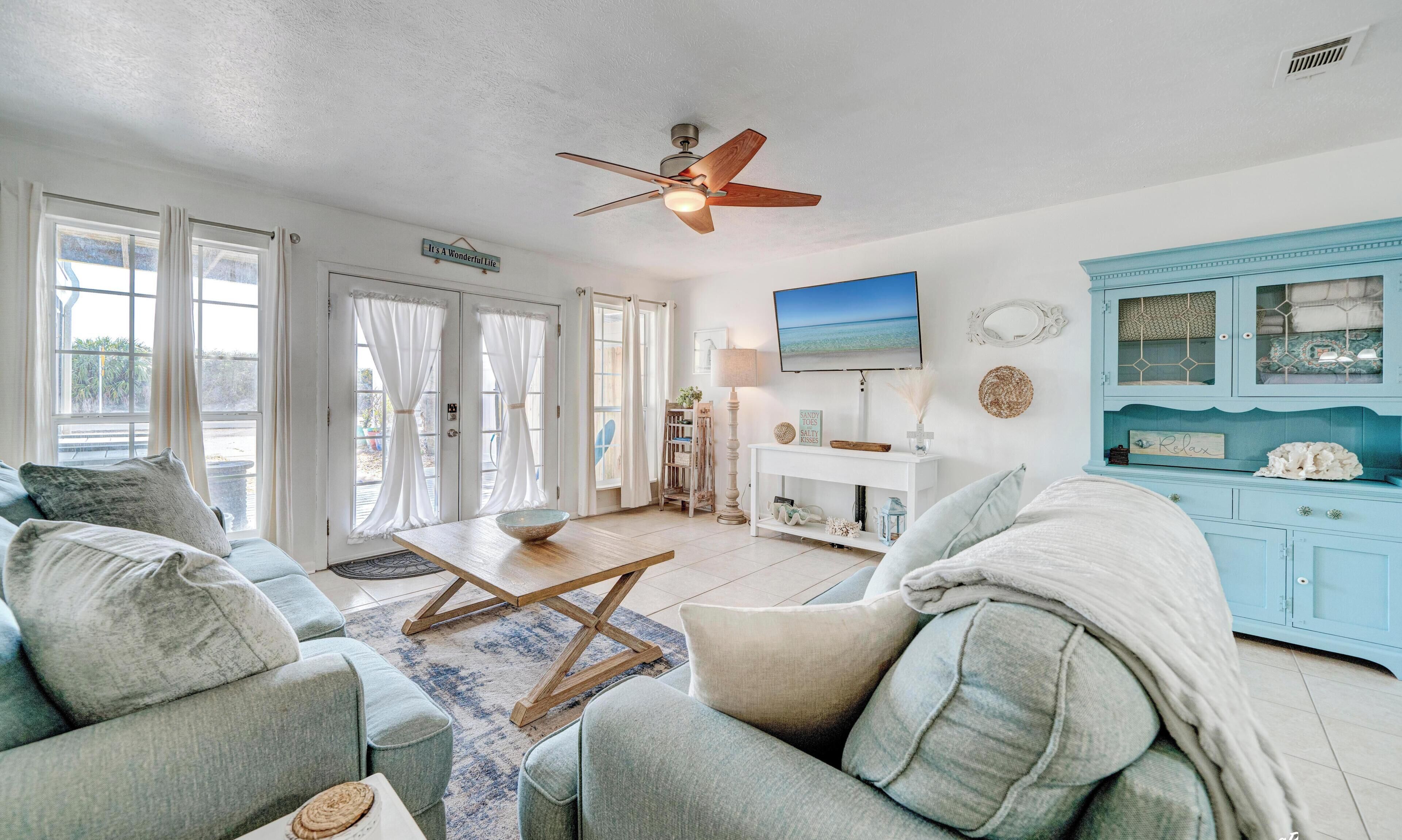 A living room with a ceiling fan, a TV, a blue cabinet, and a sign that says 'It's A Wonderful Life'.
