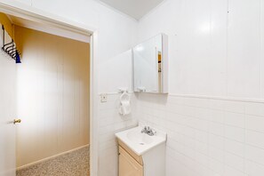 Une salle de bain avec des murs recouverts de carreaux blancs, un lavabo et un miroir.
