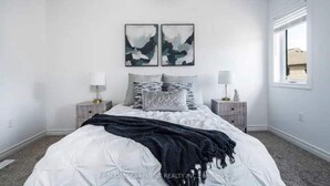 Une chambre avec un lit blanc, des oreillers gris et deux œuvres d’art abstraites accrochées au mur.