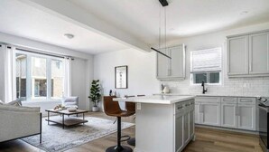 Une cuisine moderne avec des meubles blancs, un îlot central et un coin repas comprenant un canapé et des chaises.