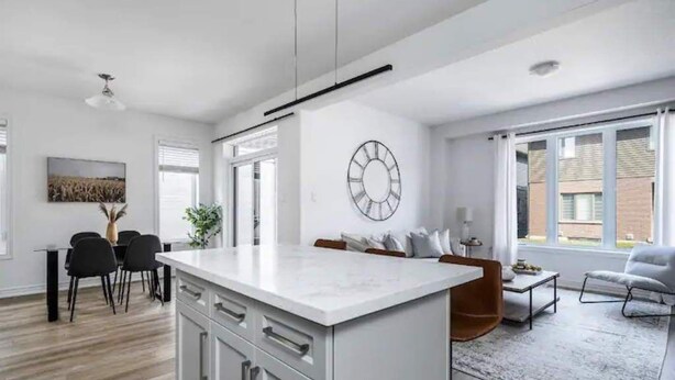 Une cuisine moderne avec des meubles blancs, un îlot central et un coin repas comprenant une table et des chaises.