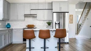 Une cuisine moderne avec des meubles blancs, un réfrigérateur en acier inoxydable et trois tabourets de bar.
