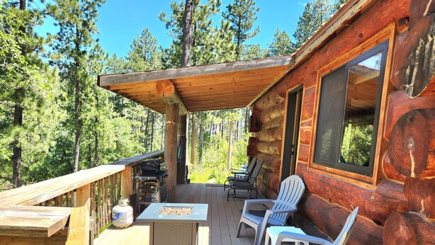 A wooden deck with outdoor seating, a grill, and a view of the forest.