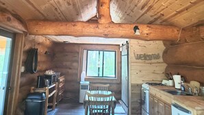 A wooden cabin interior with a dining area, kitchen, and a large window.