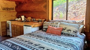 A cozy cabin interior with a wooden interior, a kitchen area, and a bed with patterned bedding.