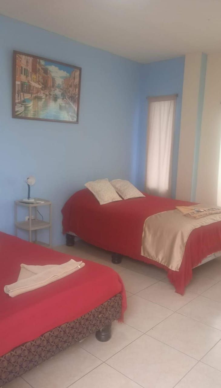 Una habitación con dos camas, un cuadro en la pared y una mesita con una lámpara.