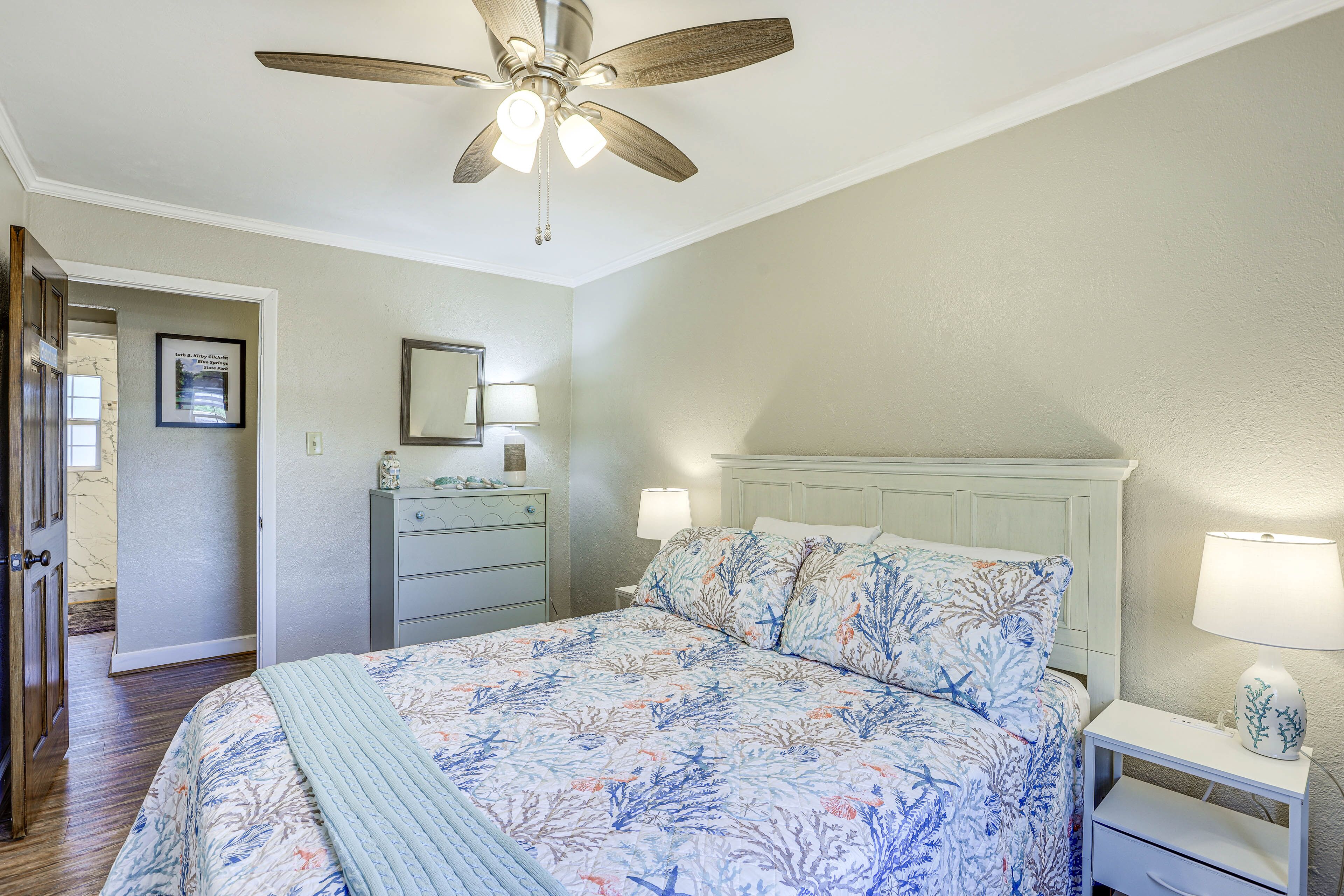 A bedroom with a bed, nightstand, dresser, ceiling fan, and a framed picture on the wall.