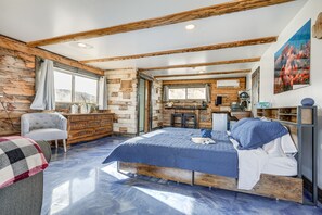 A bedroom with a wooden bed frame, a dresser, a chair, and a view of a kitchen area.
