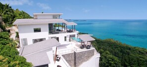 A modern multi-story house with a large balcony overlooking a turquoise sea.
