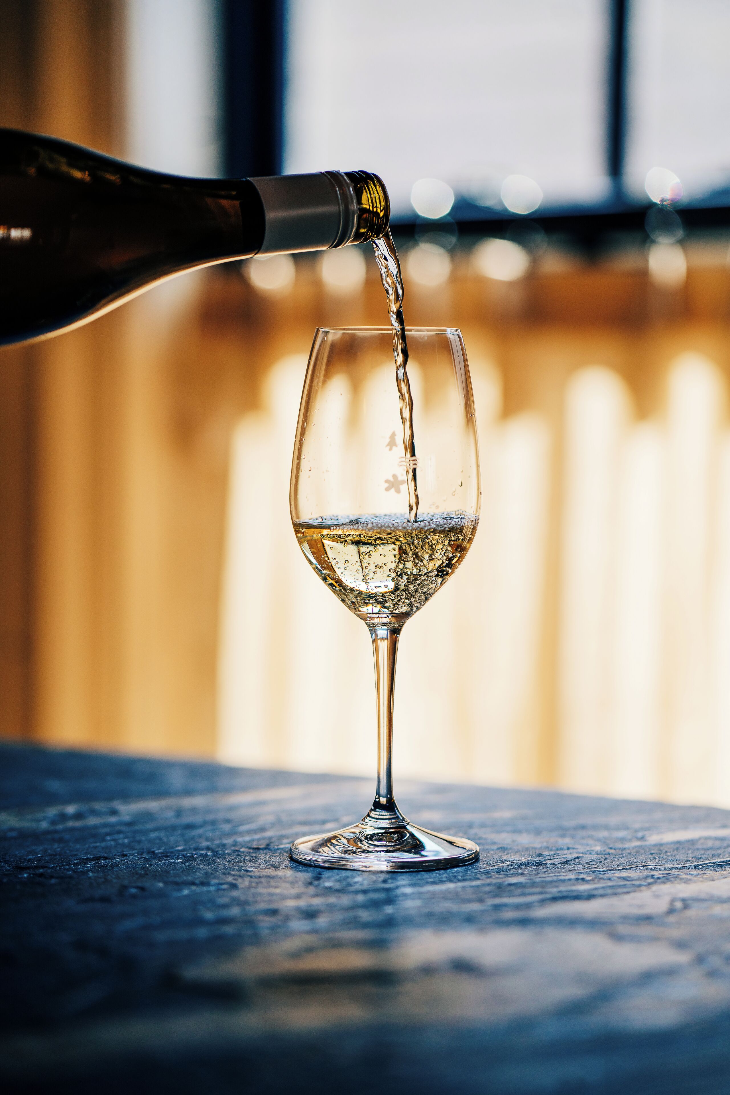 A wine glass being filled with a clear liquid, likely wine, on a textured surface.