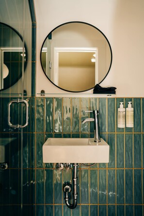 A bathroom with a white sink, a round mirror, and green tiled walls.
