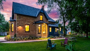 A brick house with a dark roof, a front porch, and a lawn with chairs.