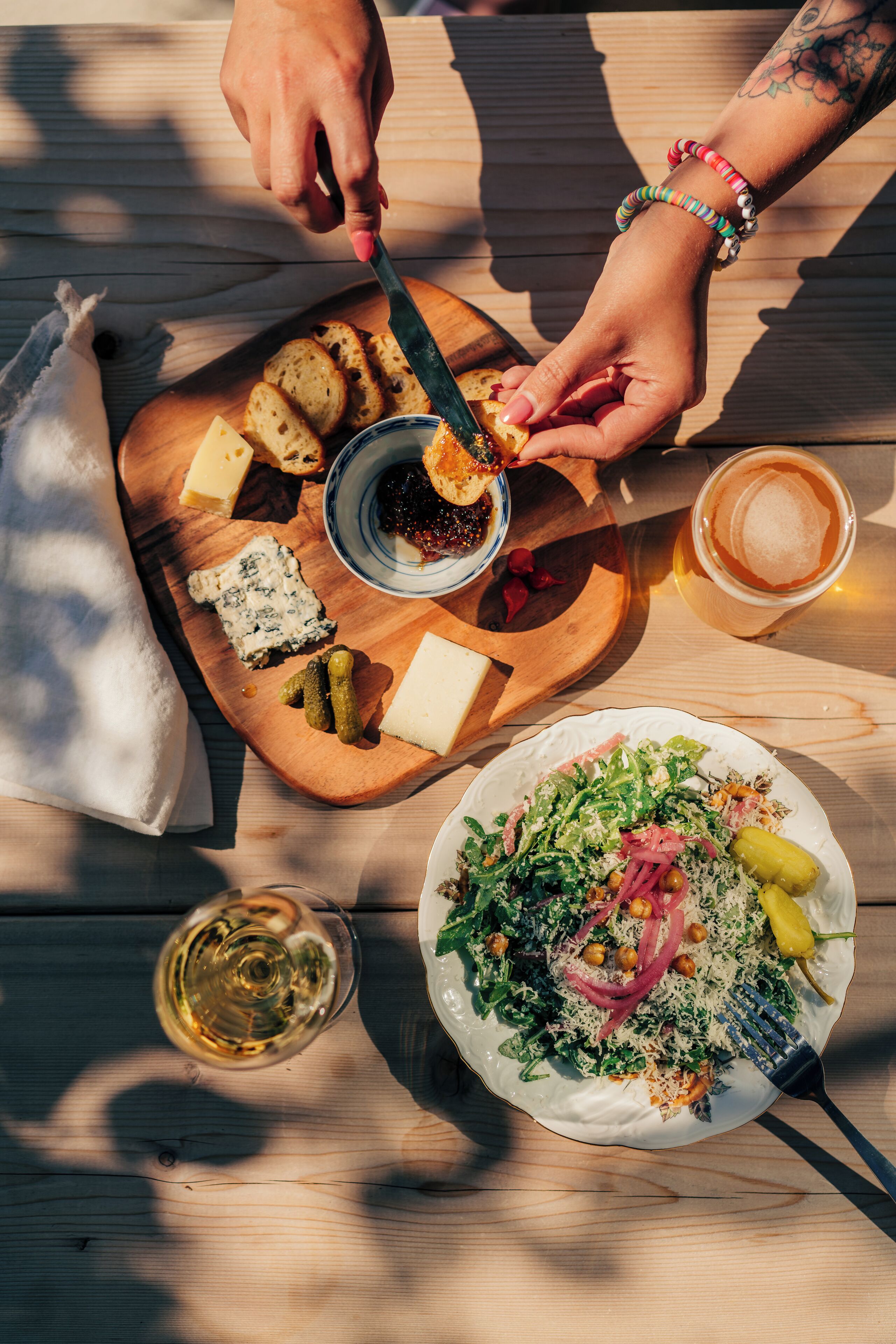 A wooden table with a variety of food items including cheese, bread, and a salad, along with glasses of wine.
