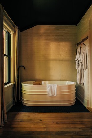 A room with a wooden floor, a bathtub, and a window with curtains.