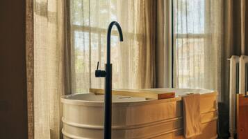 Relax in a spacious bathtub with a wall-mounted faucet, surrounded by sheer curtains and a wooden bench.