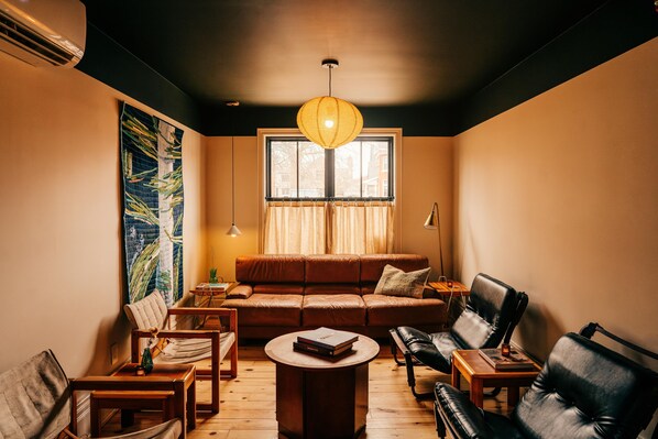 A cozy living room with a brown leather sofa, a wooden coffee table, and a hanging light fixture.