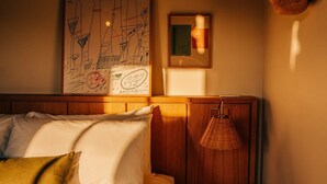 A cozy bedroom with a bed, pillows, a hanging lamp, and artwork on the wall.