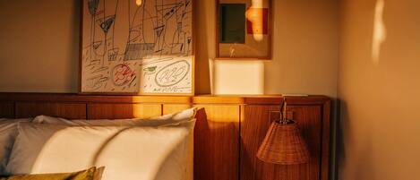 A cozy bedroom with a bed, pillows, a hanging lamp, and artwork on the wall.