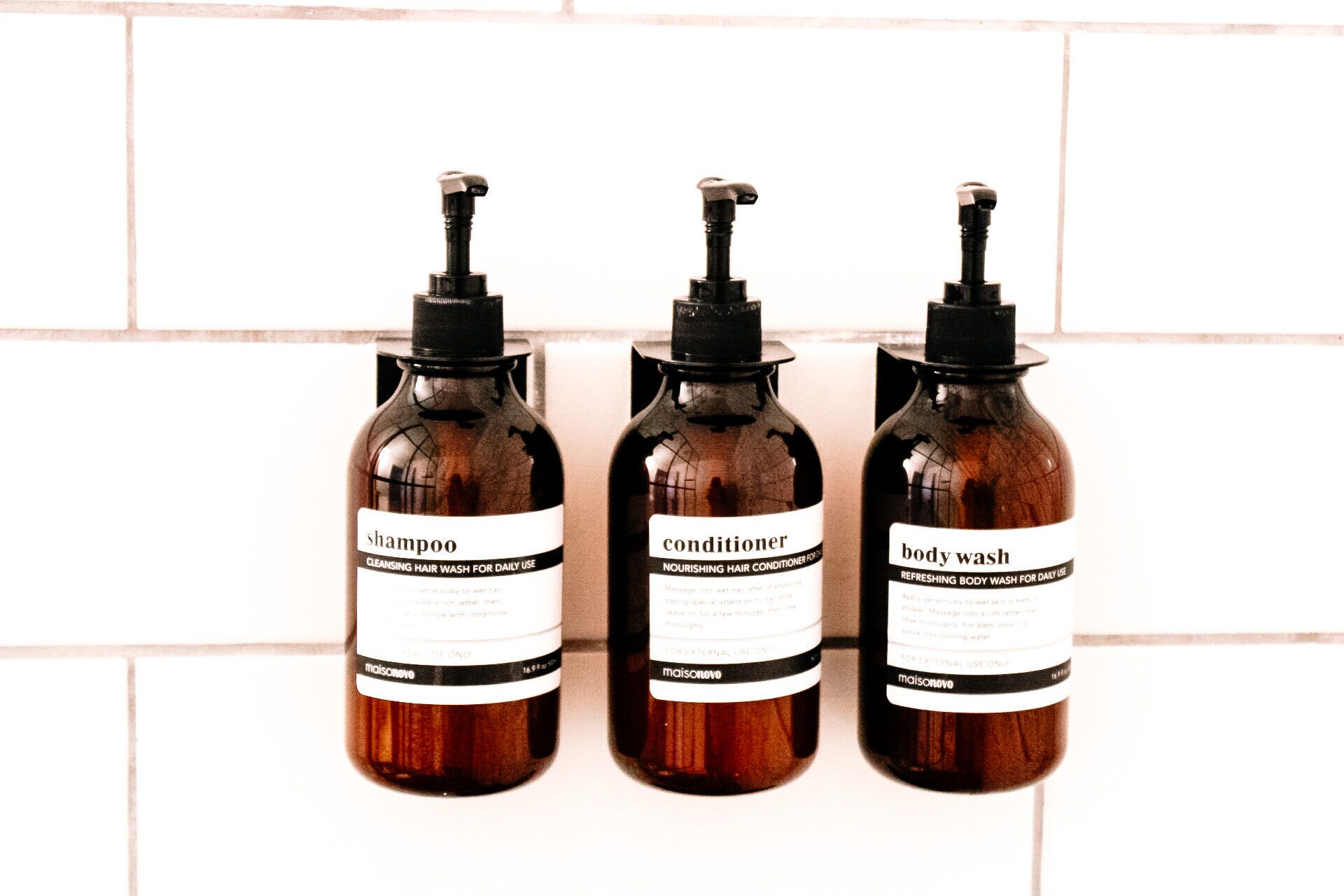 Trois flacons de produits de soins capillaires, posés contre un mur carrelé.