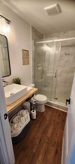 A modern bathroom with a glass-enclosed shower, a wooden vanity with a sink, and a toilet.