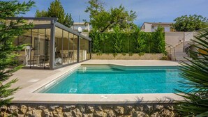 A modern outdoor swimming pool with a glass-enclosed lounge area, surrounded by greenery and stone walls. - Holiday apartment with shared-use pool (Crikvenica)