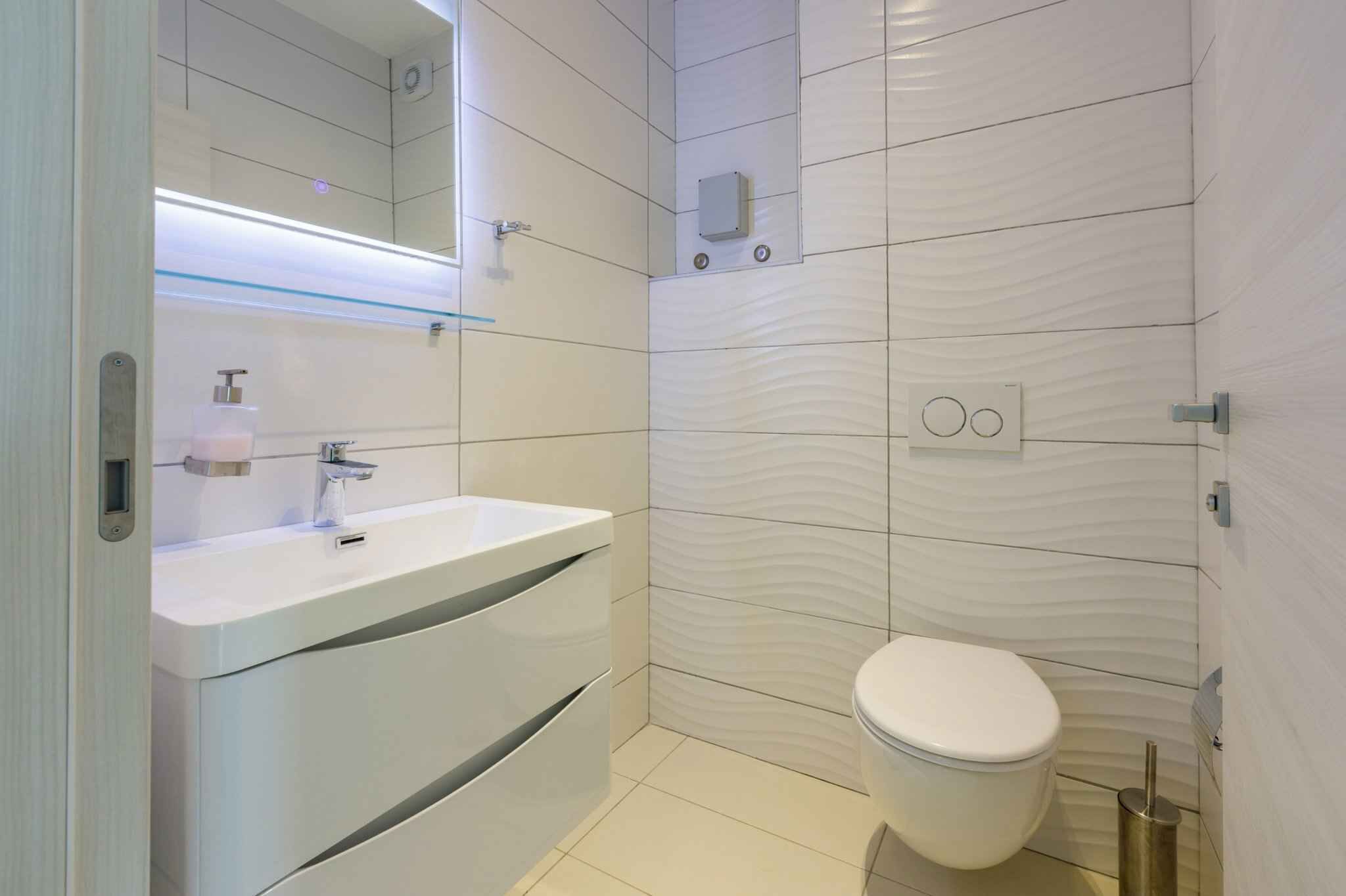 A modern bathroom with a white sink, mirror, and toilet.
