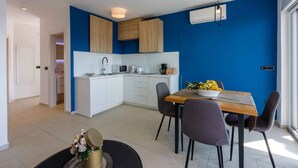 A modern kitchen with white cabinets, a microwave, and a coffee maker. There is a dining table with chairs and a bowl of fruit. - Holiday apartment with shared-use pool (Crikvenica)