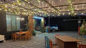 Un patio al aire libre con baldosas hexagonales, muebles de madera, plantas colgantes y luces decorativas.