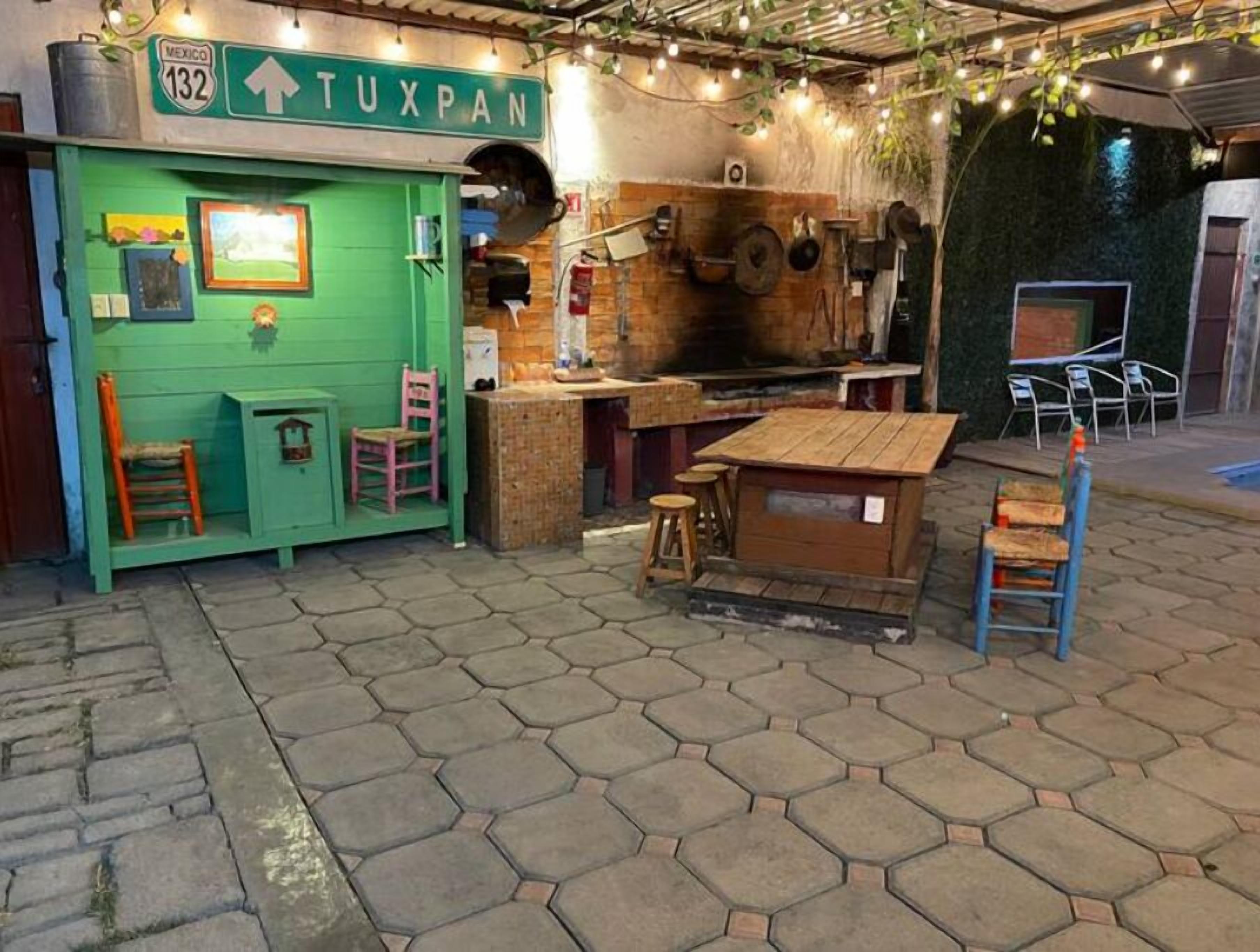 Zona d'estar a l'exterior rústica amb rajoles de pedra hexagonals, una paret verda amb un cartell que diu "TUXPAN" i diversos mobles d'exterior.