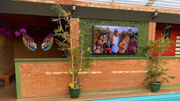 Un área de piscina con un muro de ladrillo, un letrero de neón y un mural con la imagen de un grupo de personas.