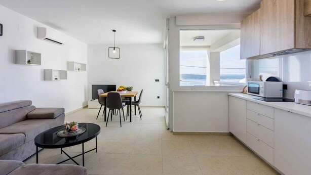 A modern, minimalist living and dining area with a sofa, dining table, and kitchenettes.
