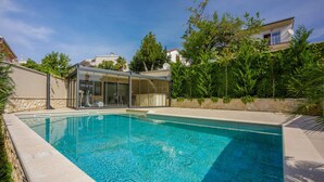 A swimming pool with a glass-enclosed area, surrounded by greenery and a stone wall.