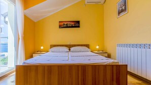 Une chambre à coucher avec un lit en bois, deux tables de chevet, un tableau représentant un paysage urbain accroché au mur et une fenêtre avec des rideaux.