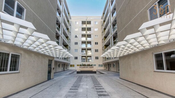 Ein modernes Gebäude mit einem zentralen Innenhof, der „Mulberry Park“ genannt wird, mit symmetrischer Gestaltung, mehreren Etagen und Balkonen.