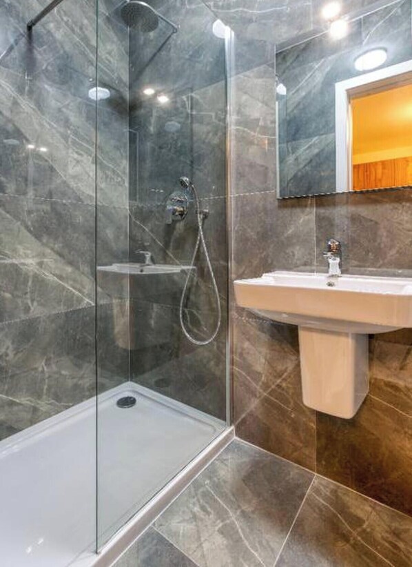 A modern bathroom with a glass shower enclosure, a marble-tiled shower area, and a sink with a mirror above it. - Modern 2BR Apt with Private Terrace & Sofa Bed (St. Paul`s Bay)