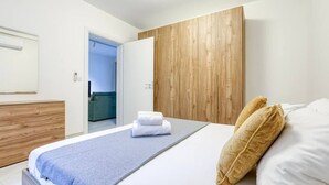 Ein modernes Hotelzimmer mit einem hölzernen Kopfteil, einem großen Bett mit weißer Bettwäsche, einer blauen Tagesdecke und einem Holzschrank.