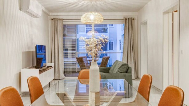 Ein moderner Essbereich mit einem Glastisch, Ledersesseln, einer Vase mit Blumen und Blick auf die Stadt durch große Fenster.