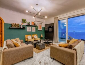 Un salon moderne avec vue sur l’océan, comprenant deux canapés, une table basse et un lustre.