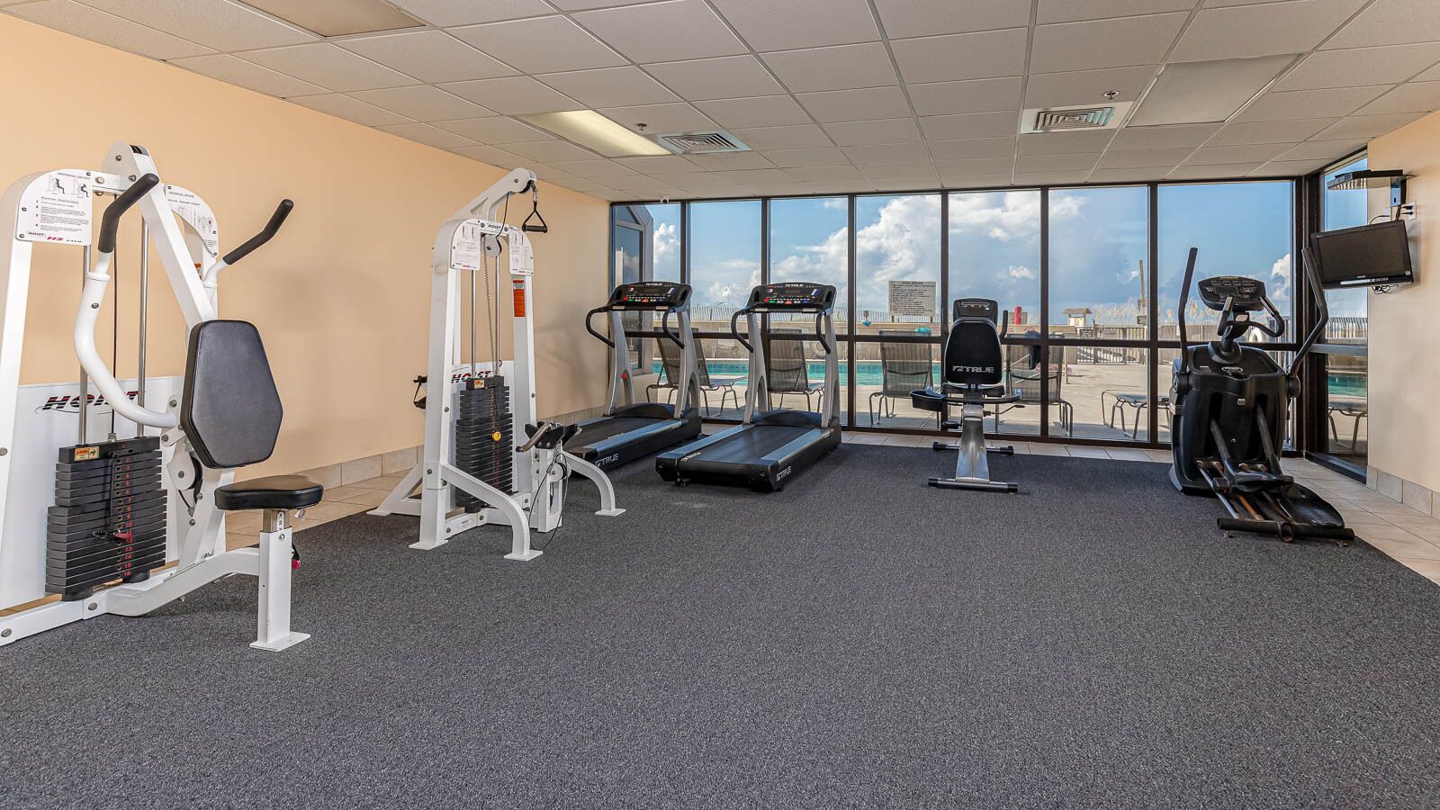 A gym with various exercise equipment, a treadmill, and a view of the city through large windows.