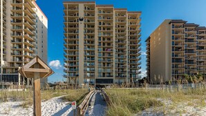 A high-rise hotel with multiple balconies, a sandy beach in the foreground, and a clear blue sky. - Stunning Views from this 15th floor one bedroom condo! (Orange)