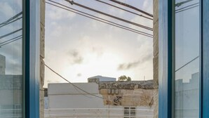 A view through a blue-framed window with a white balustrade, leading to a balcony with a stone floor. - Charming + Modern 1BR House in Historic Zebbug (Ħaż-Żebbuġ)